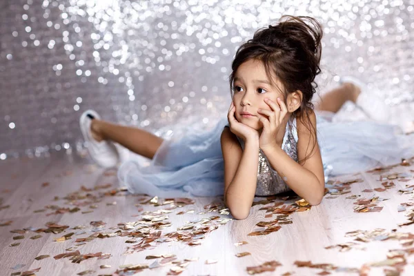 Little girl in blue dress sitting on the floor with confetti — Stock Photo, Image