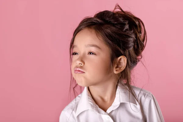 Carino orgogliosa bambina in camicia bianca su sfondo rosa. Emozioni umane ed espressione facciale — Foto Stock