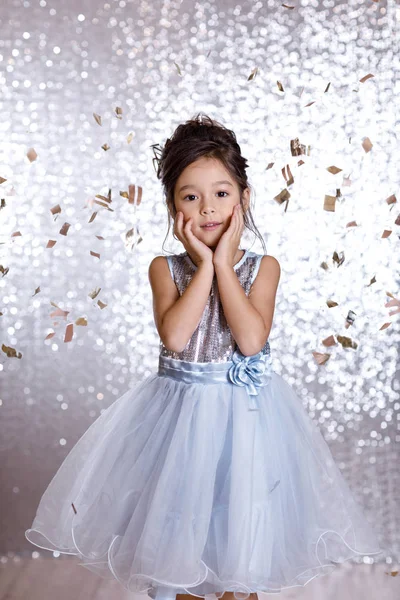 Усміхнена маленька дівчинка в срібній сукні на фоні конфетті — стокове фото