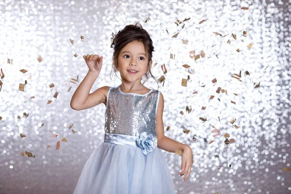 Tersenyum gadis kecil dalam gaun perak di latar belakang confetti — Stok Foto