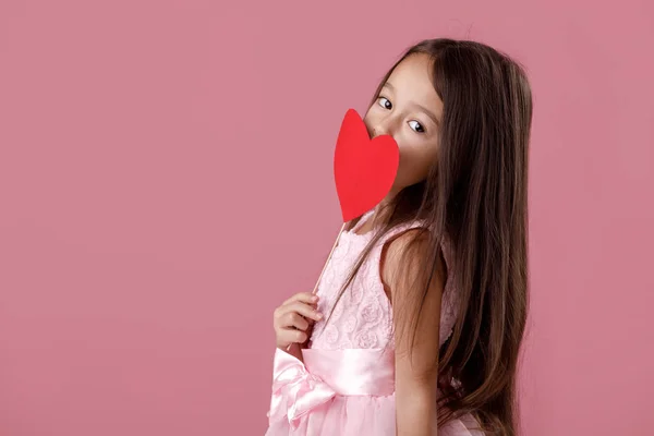 Schattig klein meisje in een roze jurk houden een papier-hart — Stockfoto