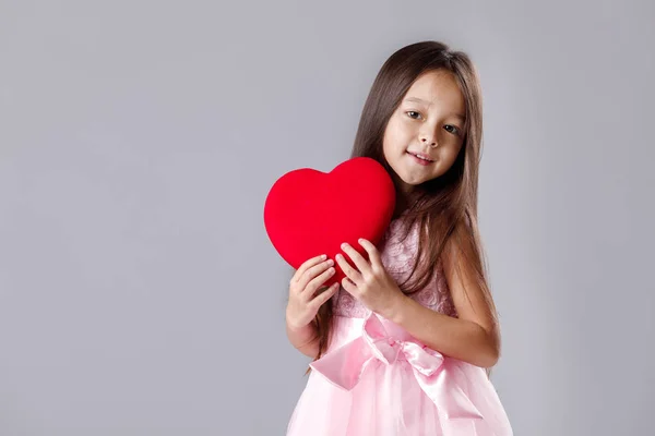 Schattig klein meisje in een roze jurk houden een papier-hart — Stockfoto