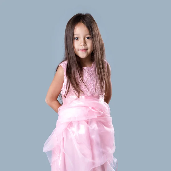 Roztomilá holčička v růžových šatech princezny na šedém pozadí. — Stock fotografie