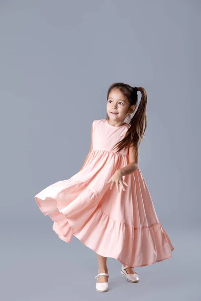 Маленька дівчинка в рожевій сукні позує на сірому фоні . — стокове фото
