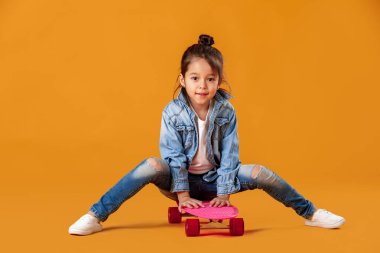 Denim içinde kaykay turuncu arka plan üzerinde şık küçük çocuk kızla