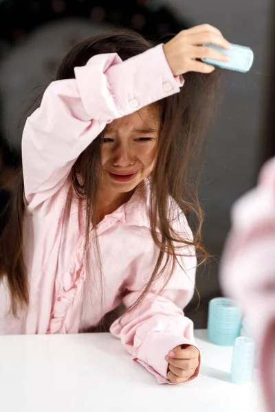 Плачущая маленькая девочка пытается удалить волосы бигуди сама — стоковое фото