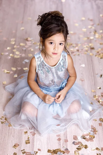 Little girl in blue dress sitting on the floor with confetti — Stock Photo, Image