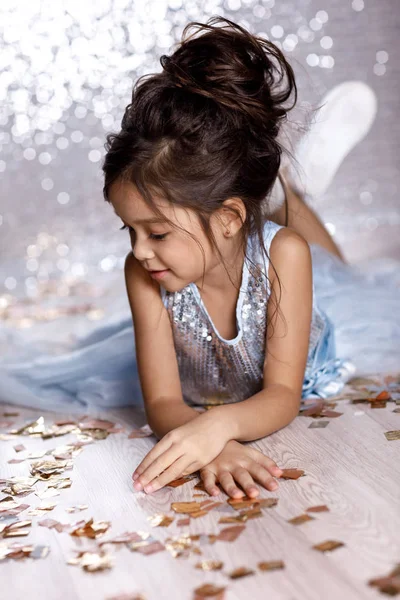 Kleines Mädchen in blauem Kleid sitzt mit Konfetti auf dem Boden — Stockfoto