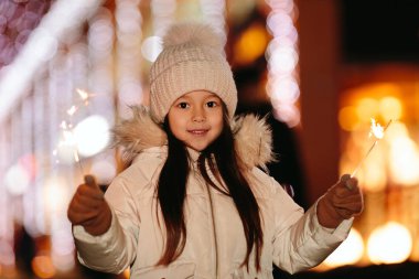 Bengal ile sevimli gülümseyen küçük kız sokakta akşam ışıklar.