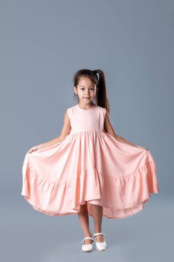 Pembe elbiseli küçük kız gri arka planda poz veriyor.