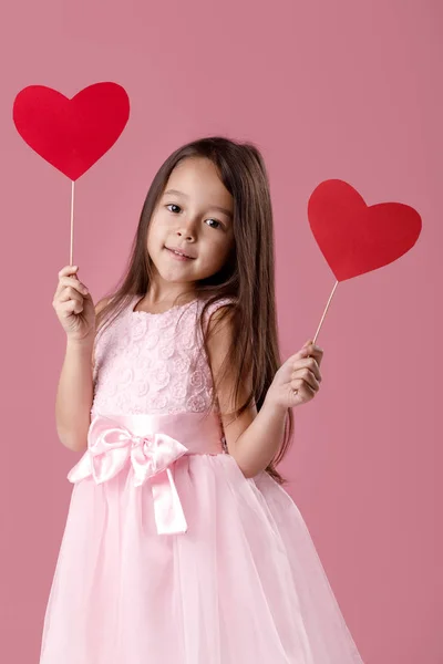 Мила маленька дівчинка в рожевій сукні тримає паперове серце — стокове фото