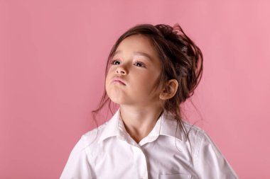 Pembe bir arka plan üzerinde beyaz gömlekli sevimli gurur küçük kız. İnsan duygu ve yüz ifadesi