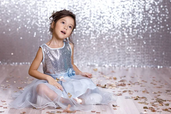Klein meisje in blauwe jurk zittend op de vloer met confetti — Stockfoto