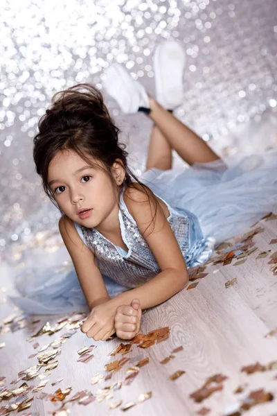 Liten flicka i blå klänning sitter på golvet med konfetti — Stockfoto