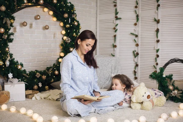 Ibu membaca buku untuk putrinya yang lucu di dekat pohon Natal — Stok Foto