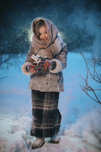 Menina com cesta vai e procura as primeiras flores sob a neve na floresta no inverno — Fotografia de Stock