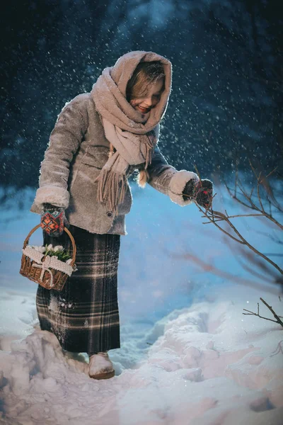 Little girl with basket goes and looks for the first flowers under the snow in forest in winter — Stock Photo, Image