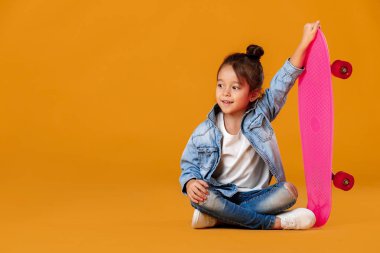 Denim içinde kaykay turuncu arka plan üzerinde şık küçük çocuk kızla