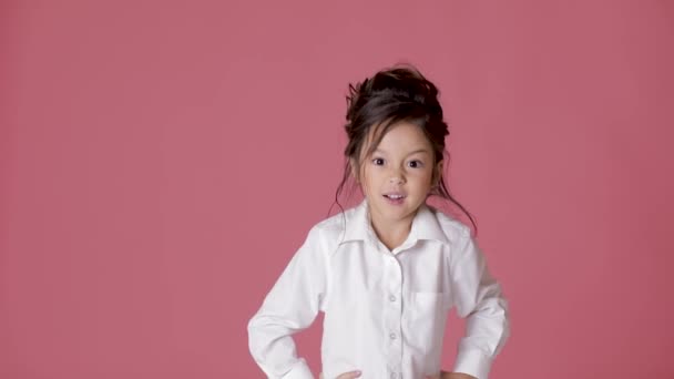 Bonito menina criança na camisa branca mostra emoções diferentes no fundo rosa . — Vídeo de Stock