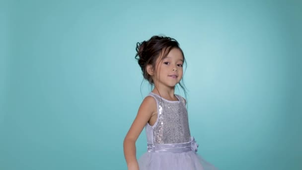 Mooi klein kind meisje in de zilveren jurk dansen op blauwe achtergrond. — Stockvideo