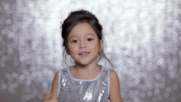 Bela menina sorrindo pequena criança em um vestido de prata dançando no fundo de bokeh prata . — Vídeo de Stock