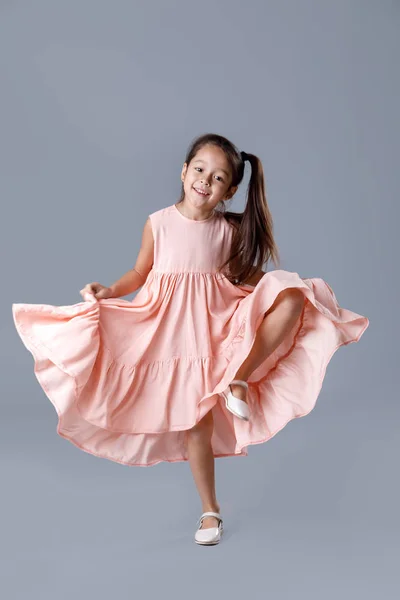 Kislány rózsaszín ruhában pózol szürke háttér. — Stock Fotó