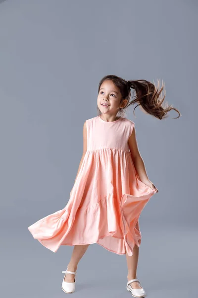 Маленька дівчинка в рожевій сукні позує на сірому фоні . — стокове фото