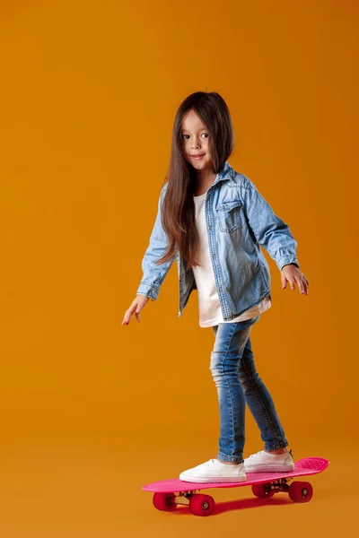 오렌지 배경에 데님에서 스케이트 보드와 세련 된 어린 아이 소녀 — 스톡 사진