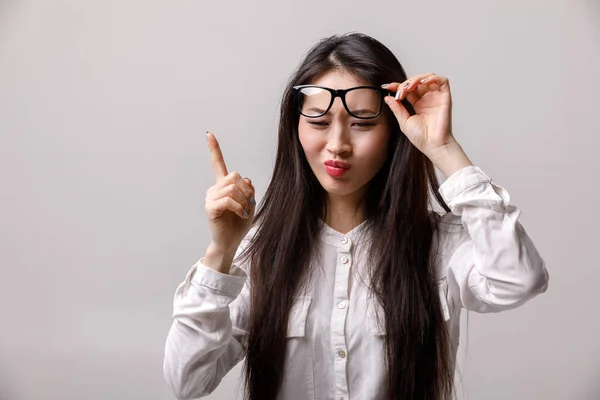 Asiatico donna in occhiali e bianco camicia avendo un buona idea su grigio sfondo — Foto Stock