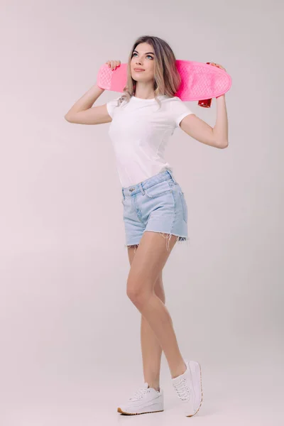 Bela mulher em t-shirt branca com skate rosa — Fotografia de Stock