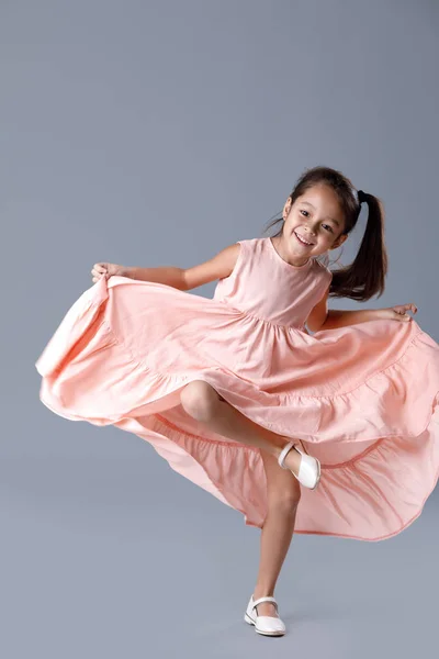 Menina em vestido rosa posando no fundo cinza. — Fotografia de Stock