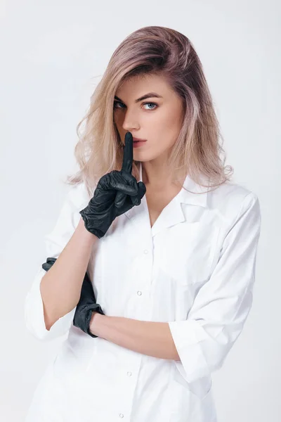 Cosmetologist in black gloves shows sign silence. Woman beautician doctor — Stock Photo, Image