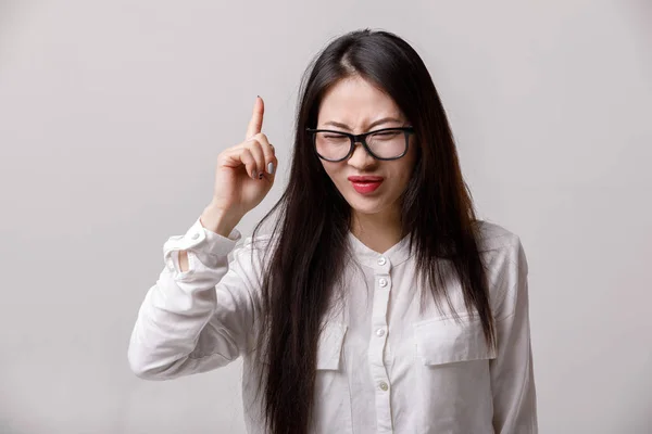 Asiatico donna in occhiali e bianco camicia avendo un buona idea su grigio sfondo — Foto Stock