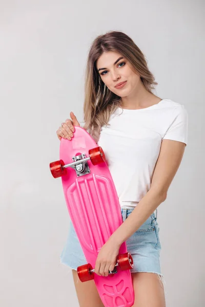 Красивая женщина в белой футболке с розовым скейтбордом — стоковое фото