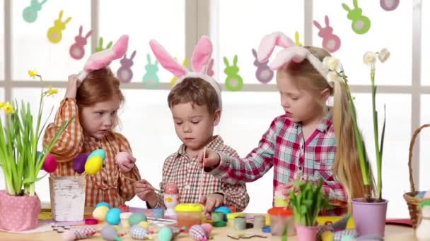 Glückliche Kinder mit Hasenohren beim Bemalen von Ostereiern. — Stockvideo