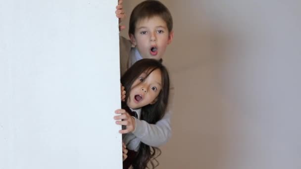 Enfants regardant par derrière la plaque blanche vierge . — Video