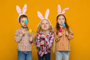 iki küçük kız ve erkek renkli yumurta tutan Paskalya bunny kulaklar ile