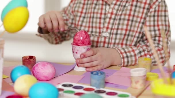 Bambino felice con le orecchie di coniglio che dipinge uova il giorno di Pasqua . — Video Stock