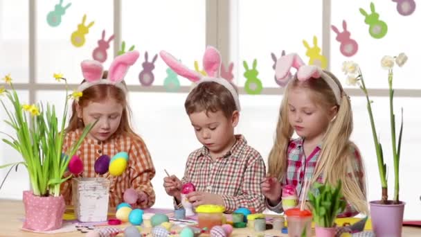 Glückliche Kinder mit Hasenohren beim Bemalen von Ostereiern. — Stockvideo