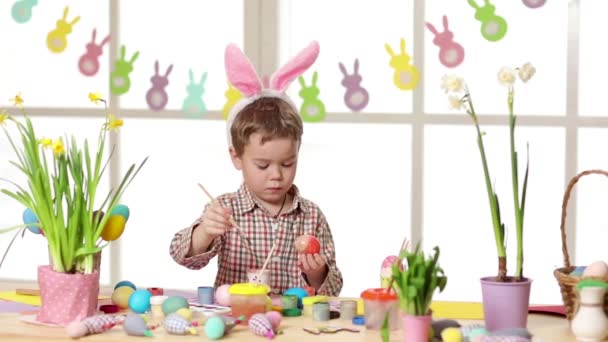 Happy child wearing bunny ears painting eggs on Easter day. — Stock Video