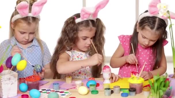 Χαρούμενα παιδιά φορώντας αυτιά λαγουδάκι ζωγραφική αυγά την ημέρα του Πάσχα. — Αρχείο Βίντεο