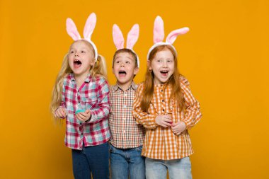 iki küçük kız ve erkek renkli yumurta tutan Paskalya bunny kulaklar ile