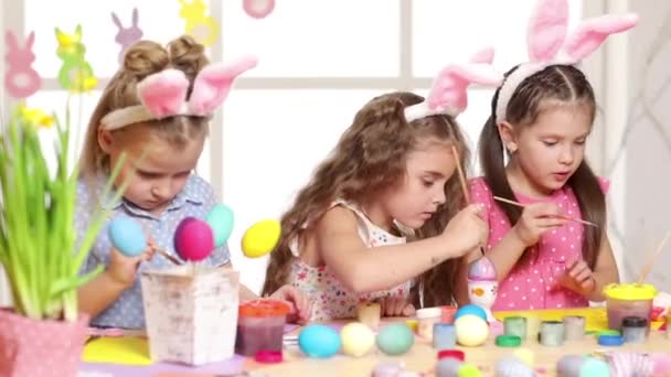 Niños felices usando orejas de conejo pintando huevos en el día de Pascua . — Vídeo de stock