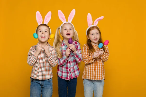 Dwa małe dziewczyny i chłopak z Easter bunny uszy gospodarstwa kolorowych jaj — Zdjęcie stockowe