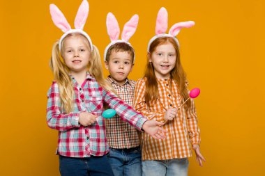 iki küçük kız ve erkek renkli yumurta tutan Paskalya bunny kulaklar ile