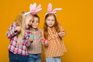 iki küçük kız ve erkek renkli yumurta tutan Paskalya bunny kulaklar ile