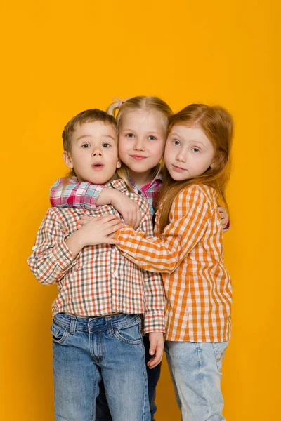 Twee kleine meisjes en jongen op een gele achtergrond — Stockfoto