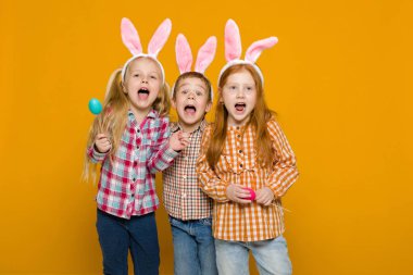 iki küçük kız ve erkek renkli yumurta tutan Paskalya bunny kulaklar ile