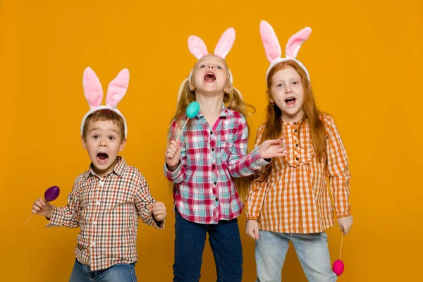 Dwa małe dziewczyny i chłopak z Easter bunny uszy gospodarstwa kolorowych jaj — Zdjęcie stockowe
