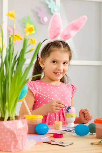 Litet barn flicka med Easter bunny öron måla påskägg hemma. — Stockfoto